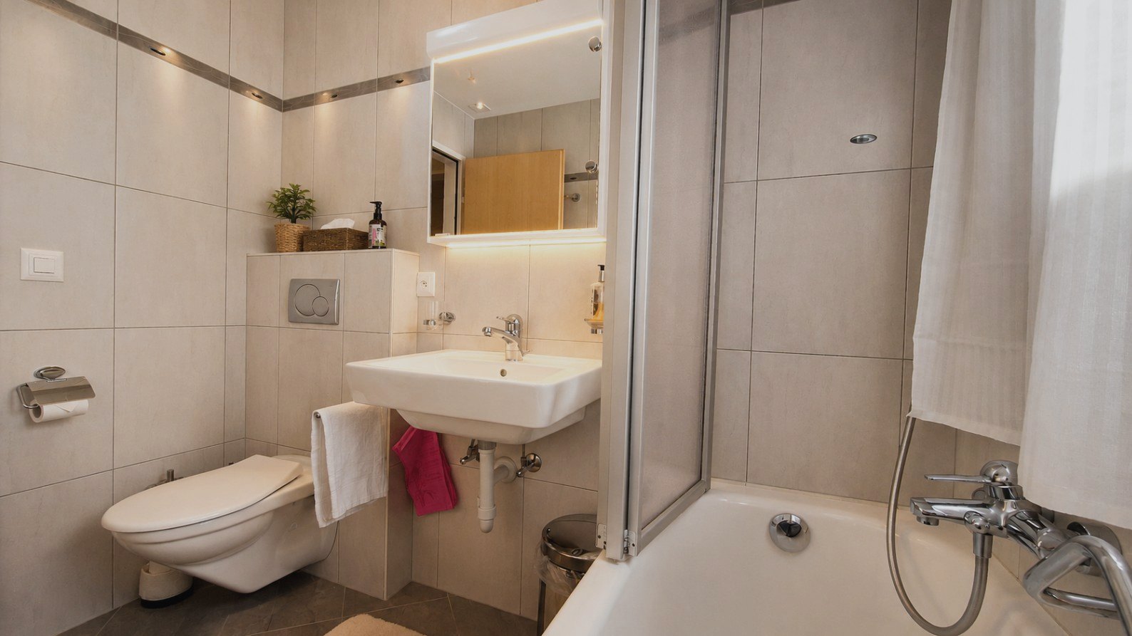 Helles Badezimmer in Auri mit Badewanne, Dusche und beleuchtetem Spiegel