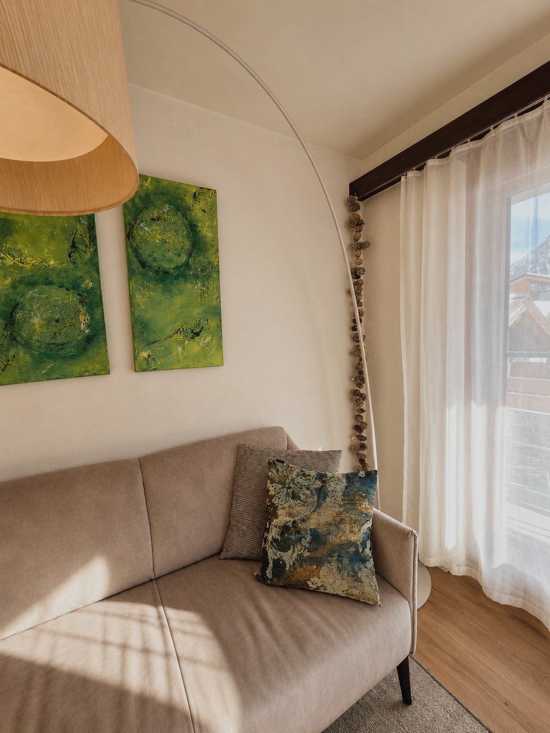 Wohnraum in Auri im Detail: Sofa mit Kissen, grüne Kunstwerke und Bogenlampe am Fenster
