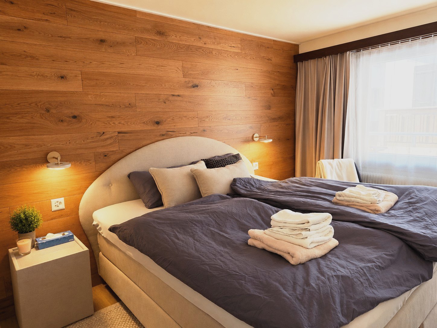 Schlafzimmer in Auri mit warmem Holzbrett-Wand, Boxspringbett und Wandleuchten