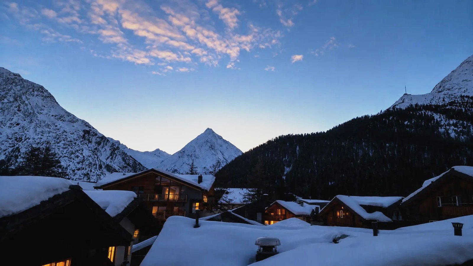 Abendstimmung über Saas-Fee: verschneite Dächer und leuchtende Fenster vor den Walliser Viertausendern