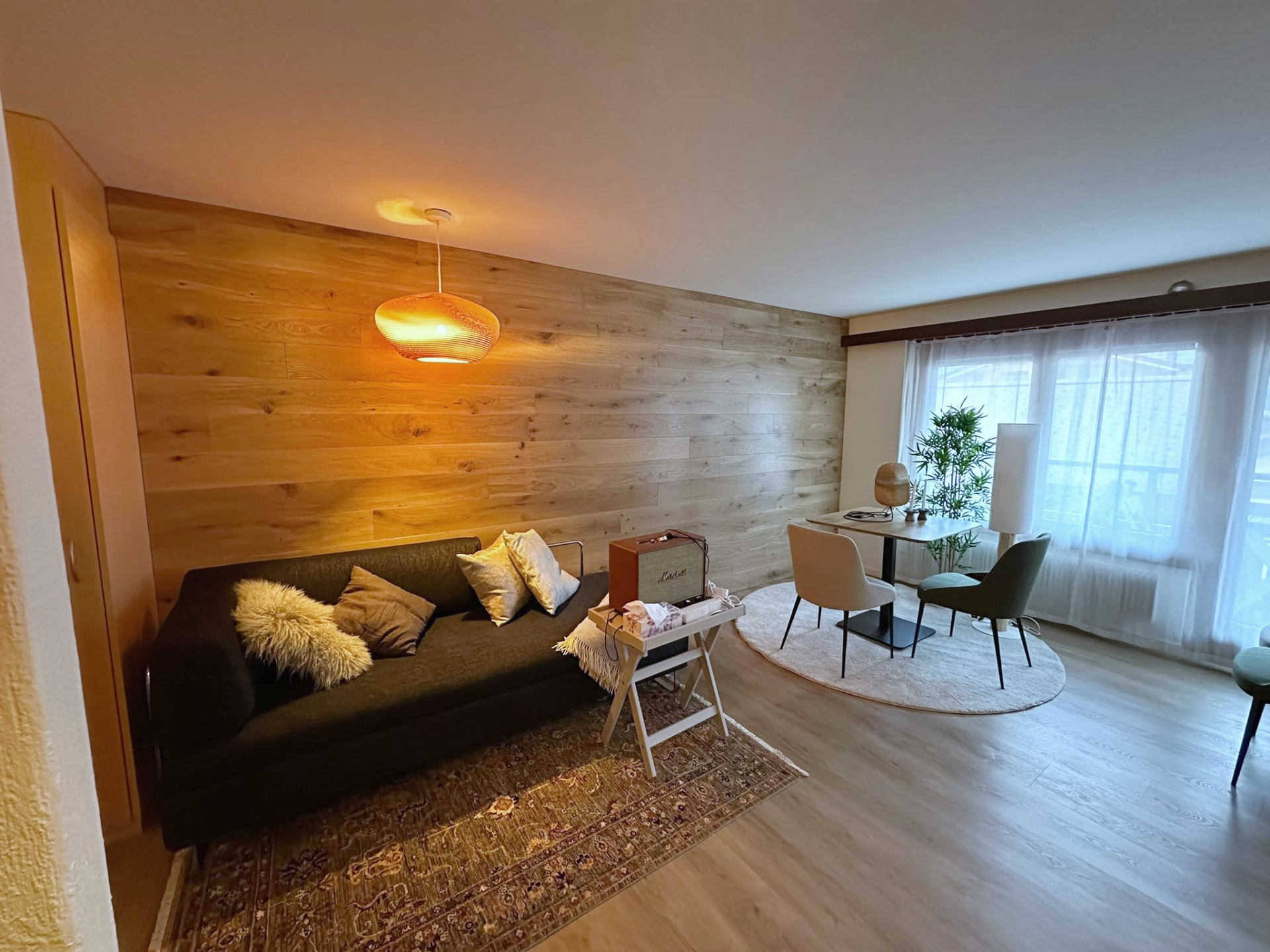 Studio Malo in Saas-Fee: Wohnbereich mit Holzwand, Sofa und Essplatz am Fenster