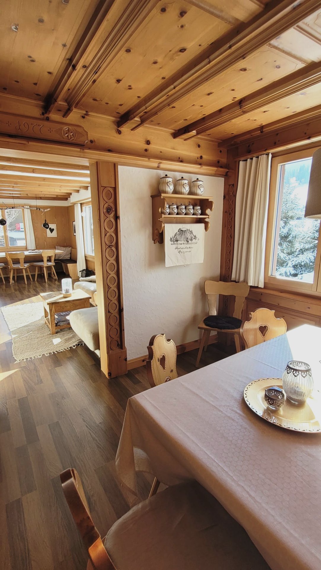 Essbereich im Chalet Nördli mit gedecktem Tisch, geschnitzten Stühlen und Blick in den Wohnraum