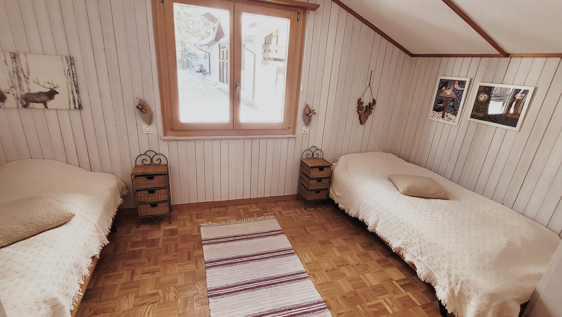 Schlafzimmer im Chalet Nördli mit zwei Einzelbetten, hellem Holzvertäfel und Blick in den Winter