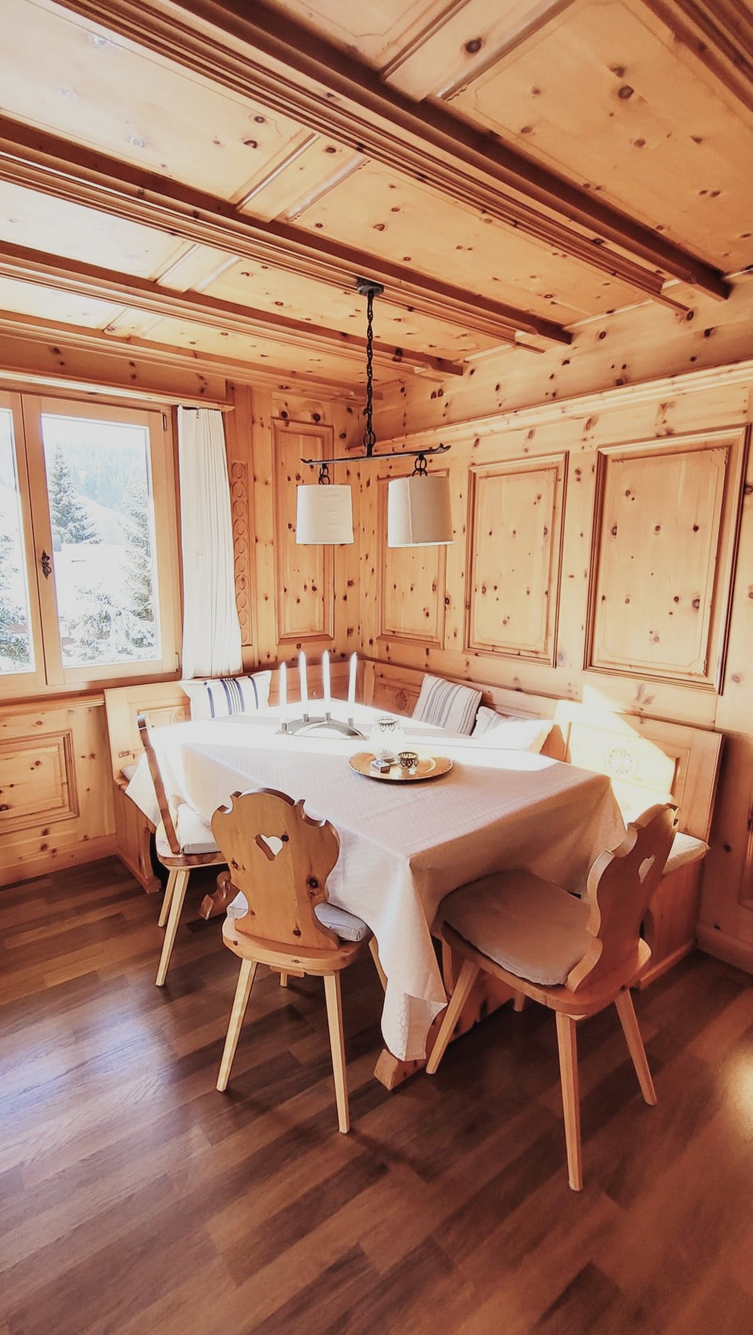 Gemütliche Essecke im Chalet Nördli mit Zirbenholz, Bank und Fensterblick in den Schnee