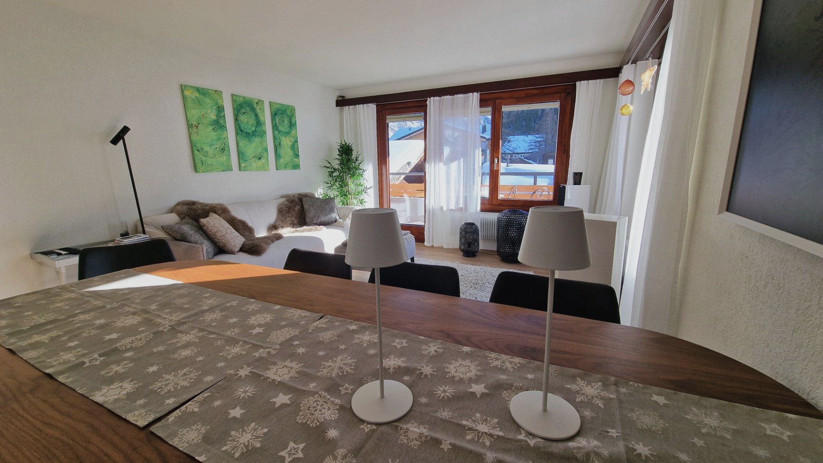 Wohnraum des Apartments in Saas-Fee mit Sofaecke, Kunstwerken und Blick auf verschneite Dächer