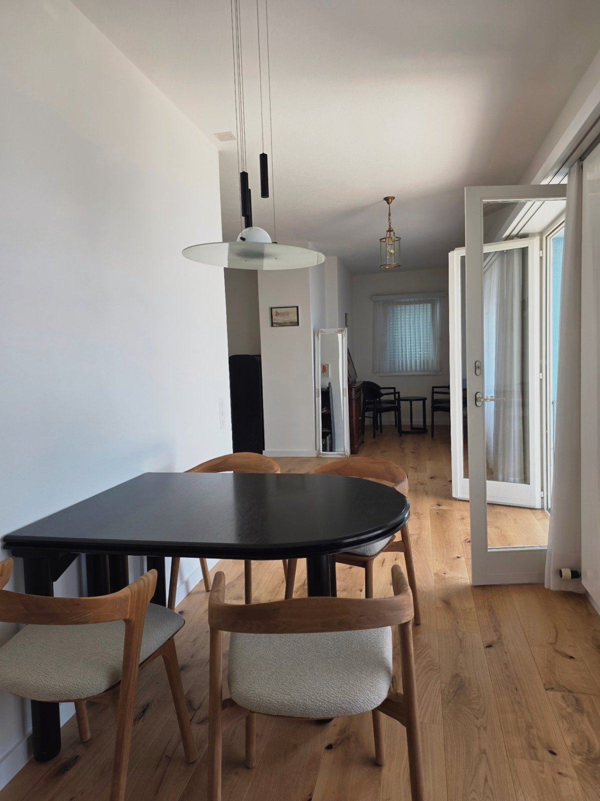 Essbereich von Soleo mit rundem schwarzen Tisch, Holzstühlen und Blick durch die Wohnung